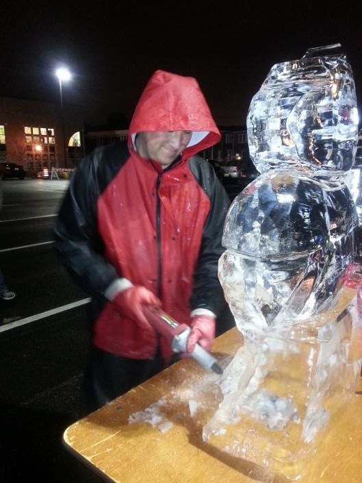 Person in red hooded jacket carving a clear ice sculpture with a chisel at night