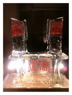 Clear glass sculpture with two red-topped columns and the word “RHYTHM” on the base