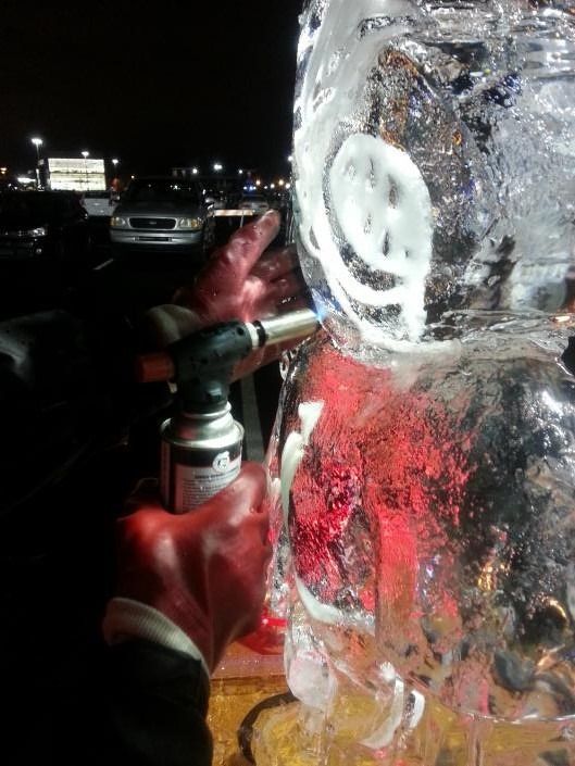 Firefighter in red gloves spraying water onto a large ice-covered surface at night.