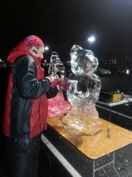 Person in a red jacket carving a transparent ice sculpture at night outdoors
