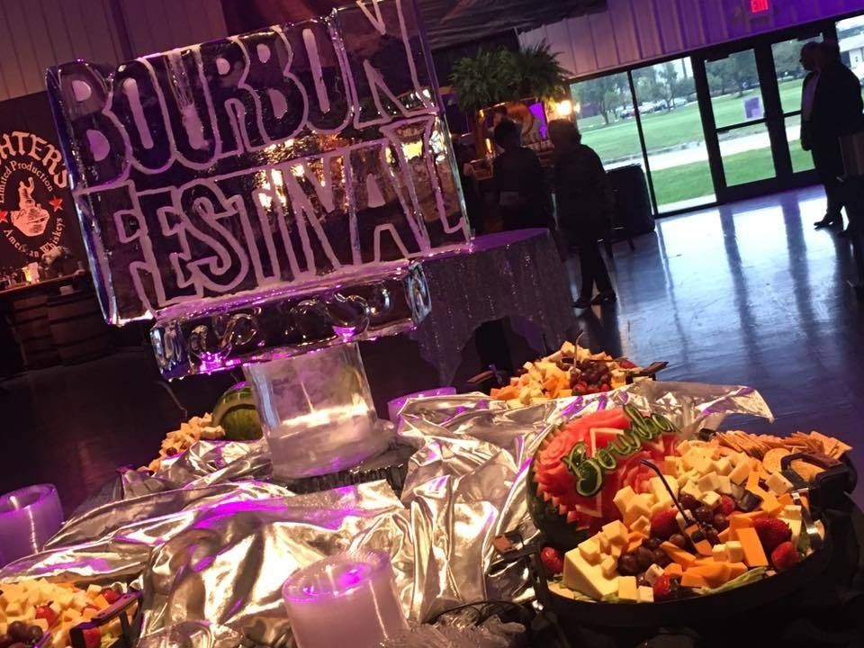 Buffet table at a Bourbon Festival with foil-covered dishes and fruit bowls under purple lighting