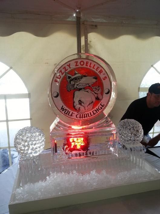 Ice sculpture display of a circular logo with glowing red light under a tent, flanked by two textured ice spheres.
