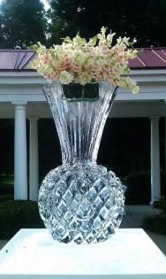 Crystal vase with pink flowers on a white pedestal outdoors in front of a house