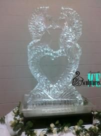 Heart-shaped ice sculpture on a pedestal, lit from below, with floral decoration at the base.