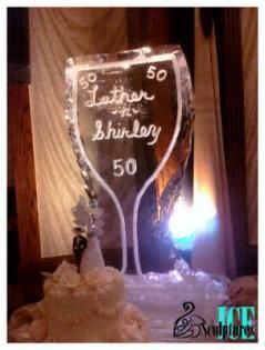 Ice sculpture champagne flute with “50” and “Happy Birthday” lit by a bright candle in a dim room
