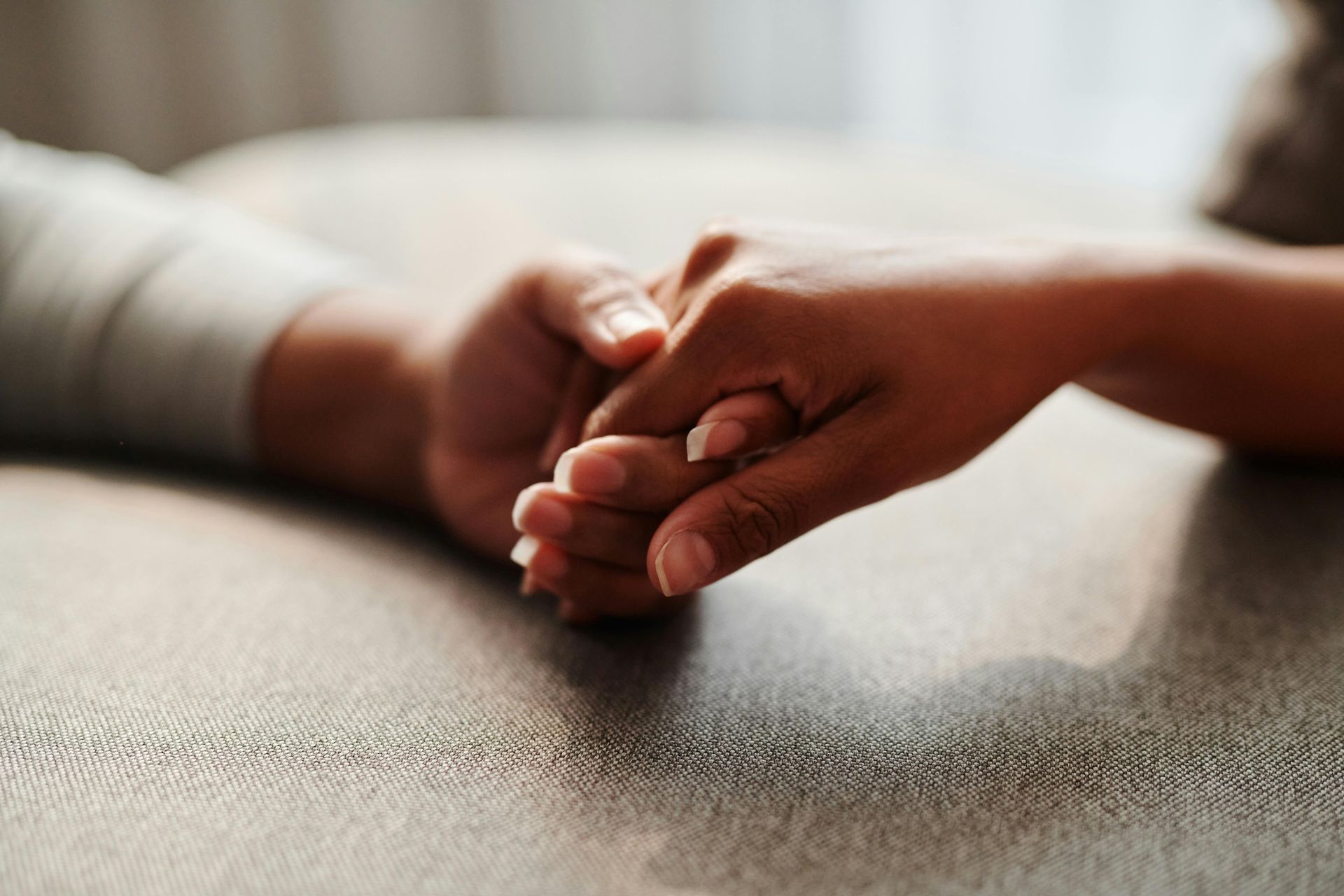 Two hands holding each other gently on a textured surface, conveying comfort and support.