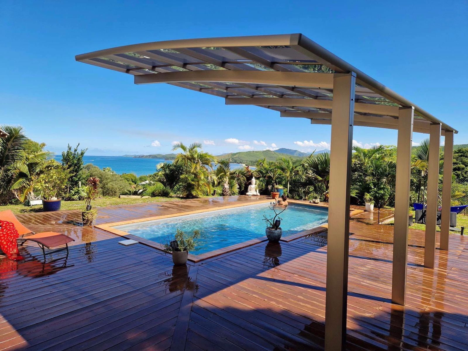 Une grande piscine est entourée d'une terrasse en bois et d'une pergola.