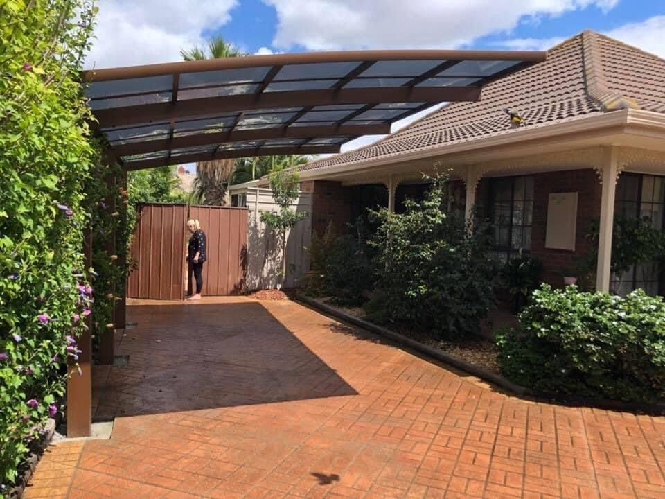 Une femme se tient devant une maison avec un abri pour voiture.