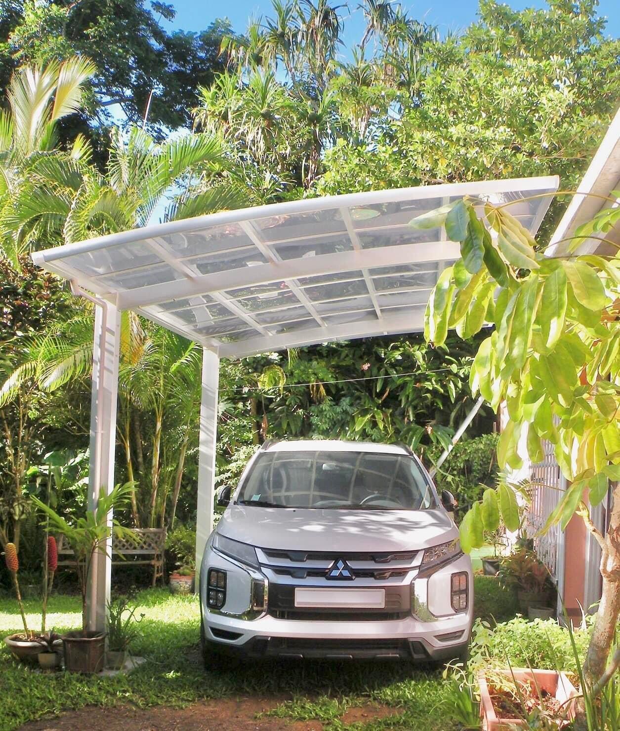 Une voiture blanche est garée sous un auvent dans une cour arrière.