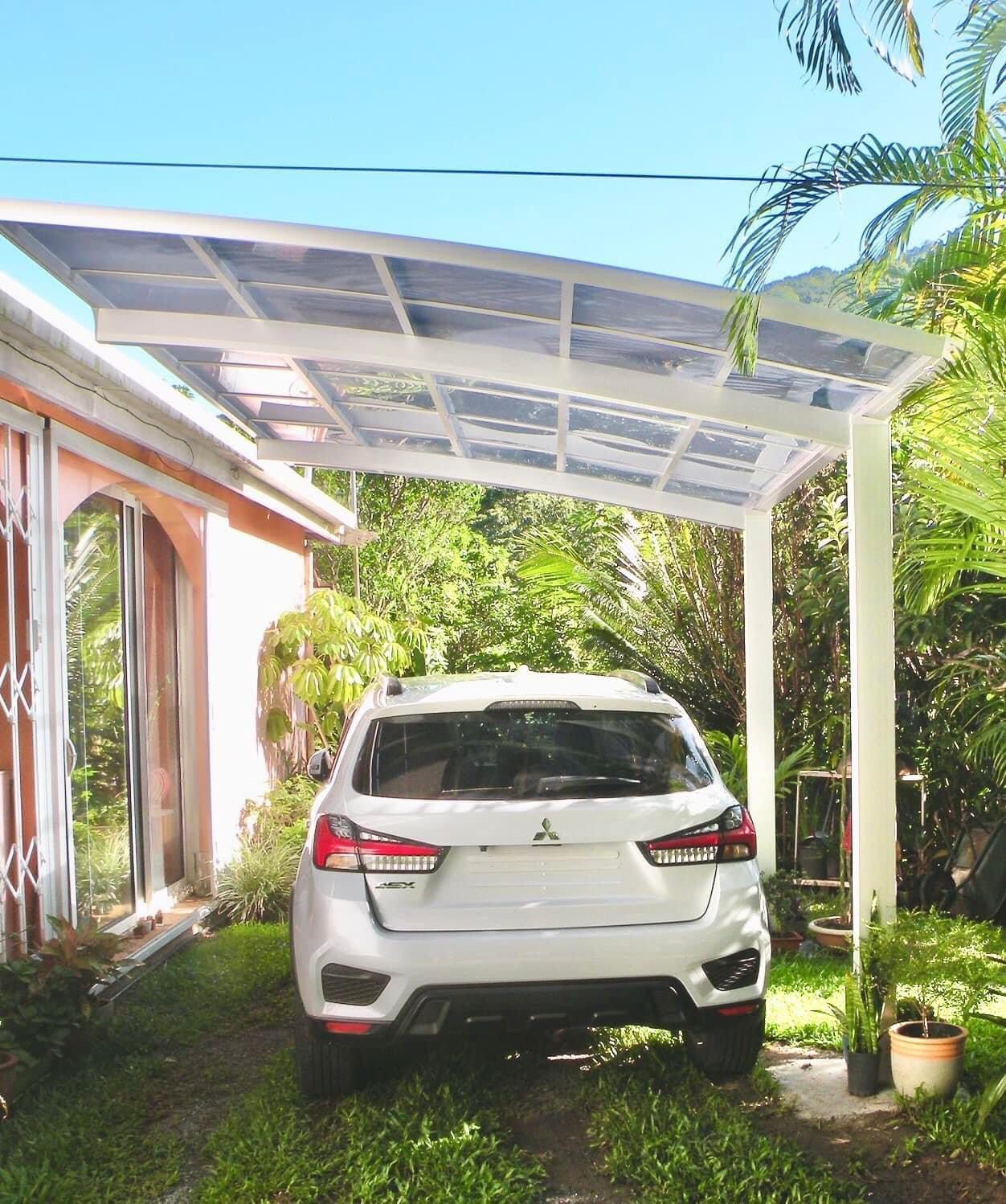 Une voiture blanche est garée sous un auvent devant une maison.