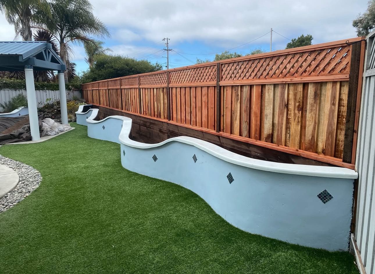 Curved gray wall with brown wooden fence and green grass.