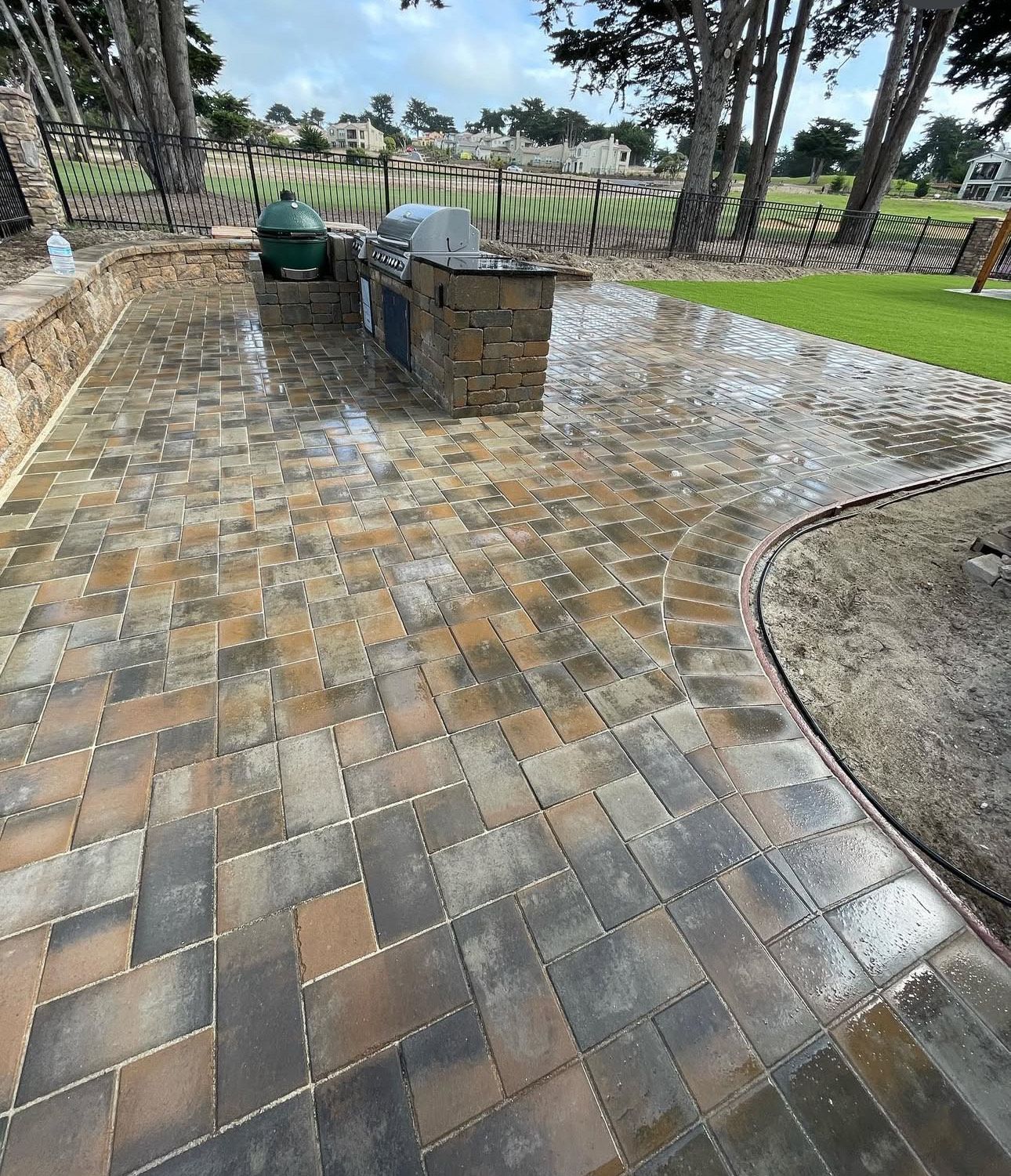 Patio with brick pavers, outdoor kitchen, and lawn in the background.