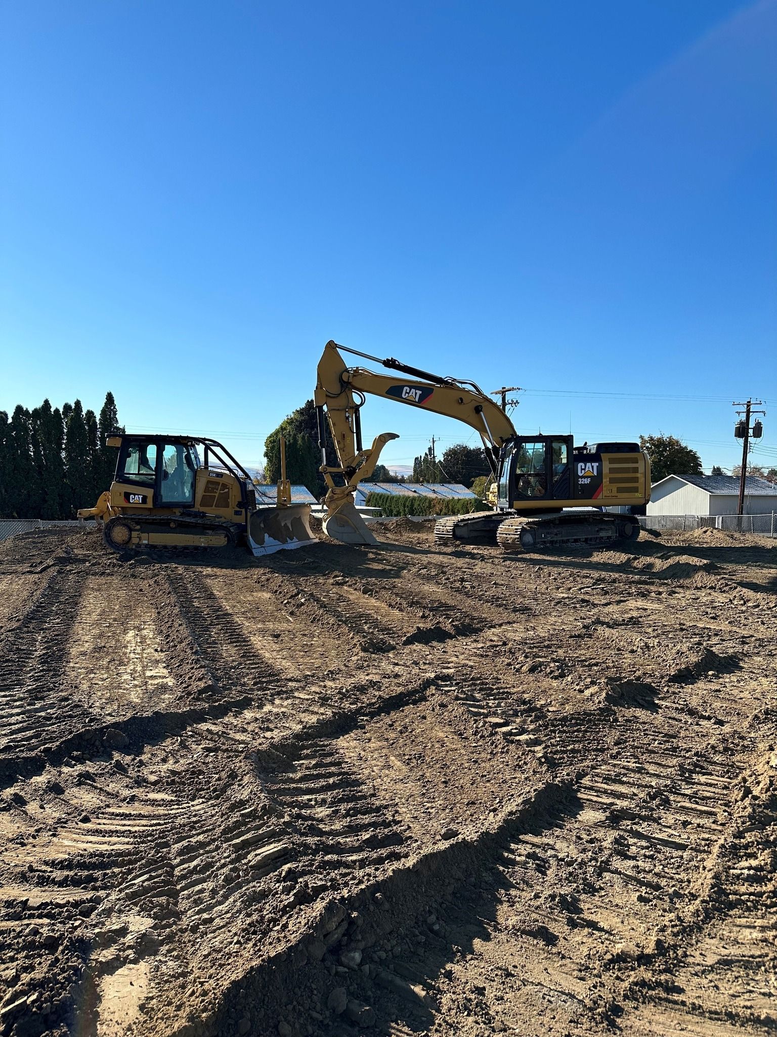 Construction site with bulldozer and excavator on dirt under a blue sky.