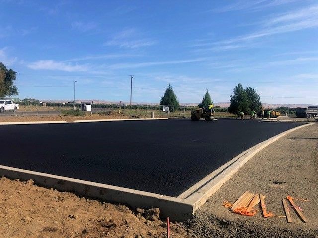 Newly paved asphalt parking lot with concrete border, under a blue sky.