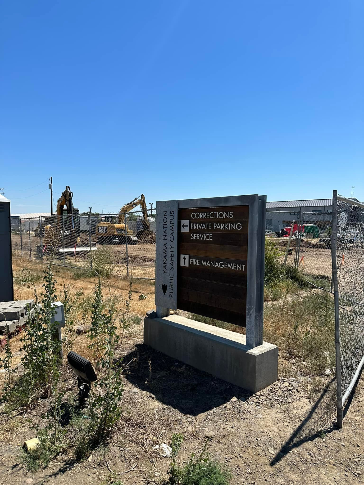 Sign with text in a construction zone under a blue sky, heavy machinery in the background.