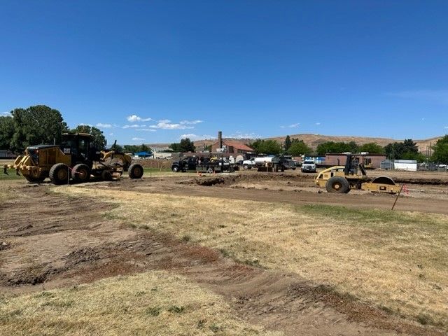 Construction site with heavy machinery grading dirt under a clear blue sky.