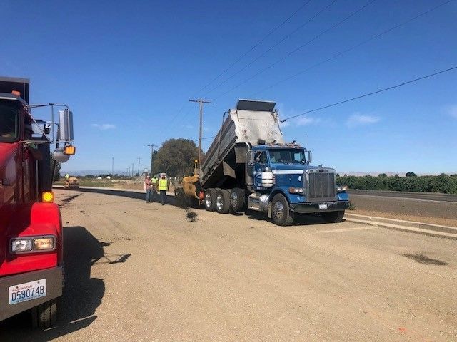 Blue dump truck unloading asphalt onto road under construction, sunny day.