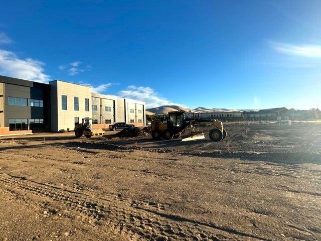 Construction site with bulldozers in front of a modern building under a blue sky.