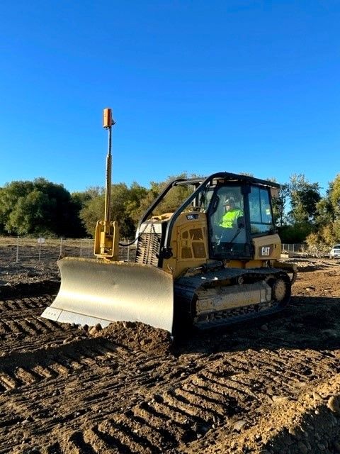 Yellow bulldozer on a construction site; operator in the cab, working under a clear blue sky.