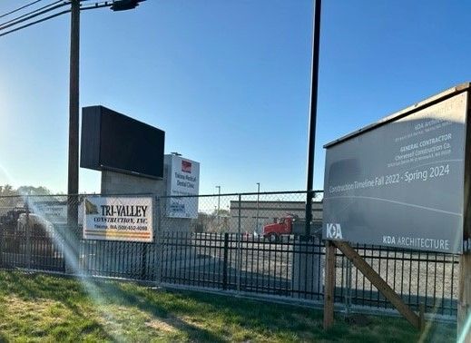 Signage for a project, with a large digital screen, on a sunny day. A construction truck is visible in the background.