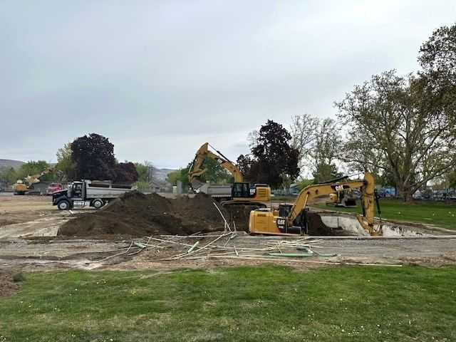 Construction site with excavators, a dump truck, and piles of dirt.