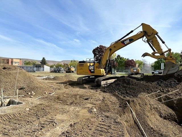 Yellow excavator digging dirt at a construction site on a sunny day.