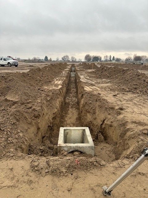 Construction site with an open trench, concrete box, and dirt, overcast sky.