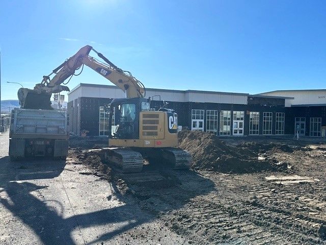 Excavator loading dirt into a dump truck at a building construction site on a sunny day.