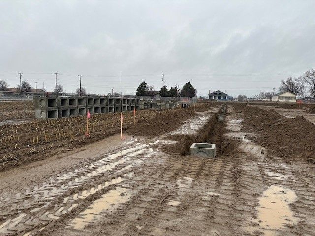 Muddy construction site with concrete blocks, ditches, and a cloudy sky.