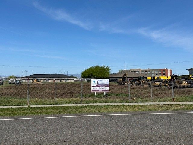Open field with a construction sign, buildings, and a clear sky.