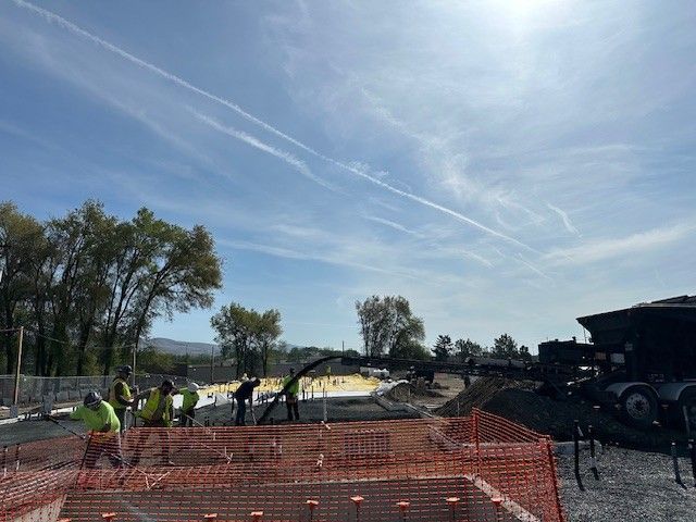 Construction workers pouring concrete on a construction site under a bright blue sky with contrails.
