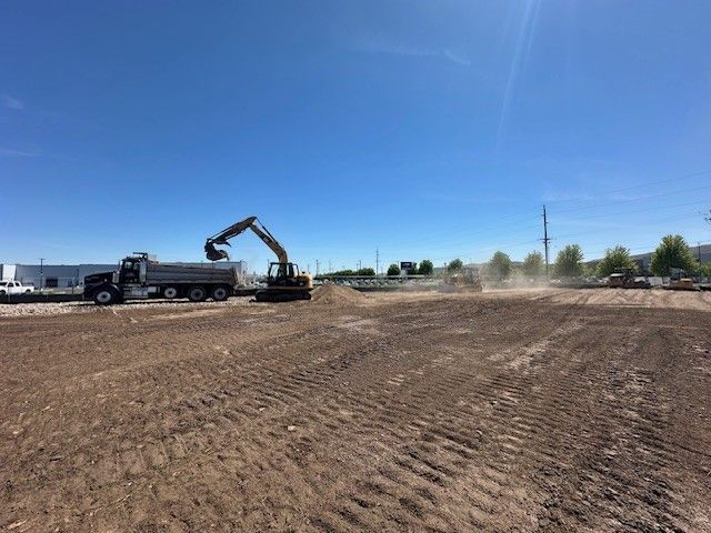 Excavator loading a dump truck on a construction site with clear blue sky.