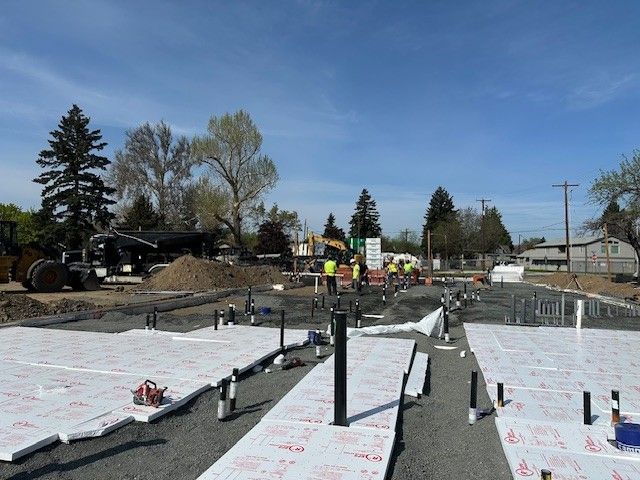 Construction site with workers, equipment, and foundation preparations under a blue sky.