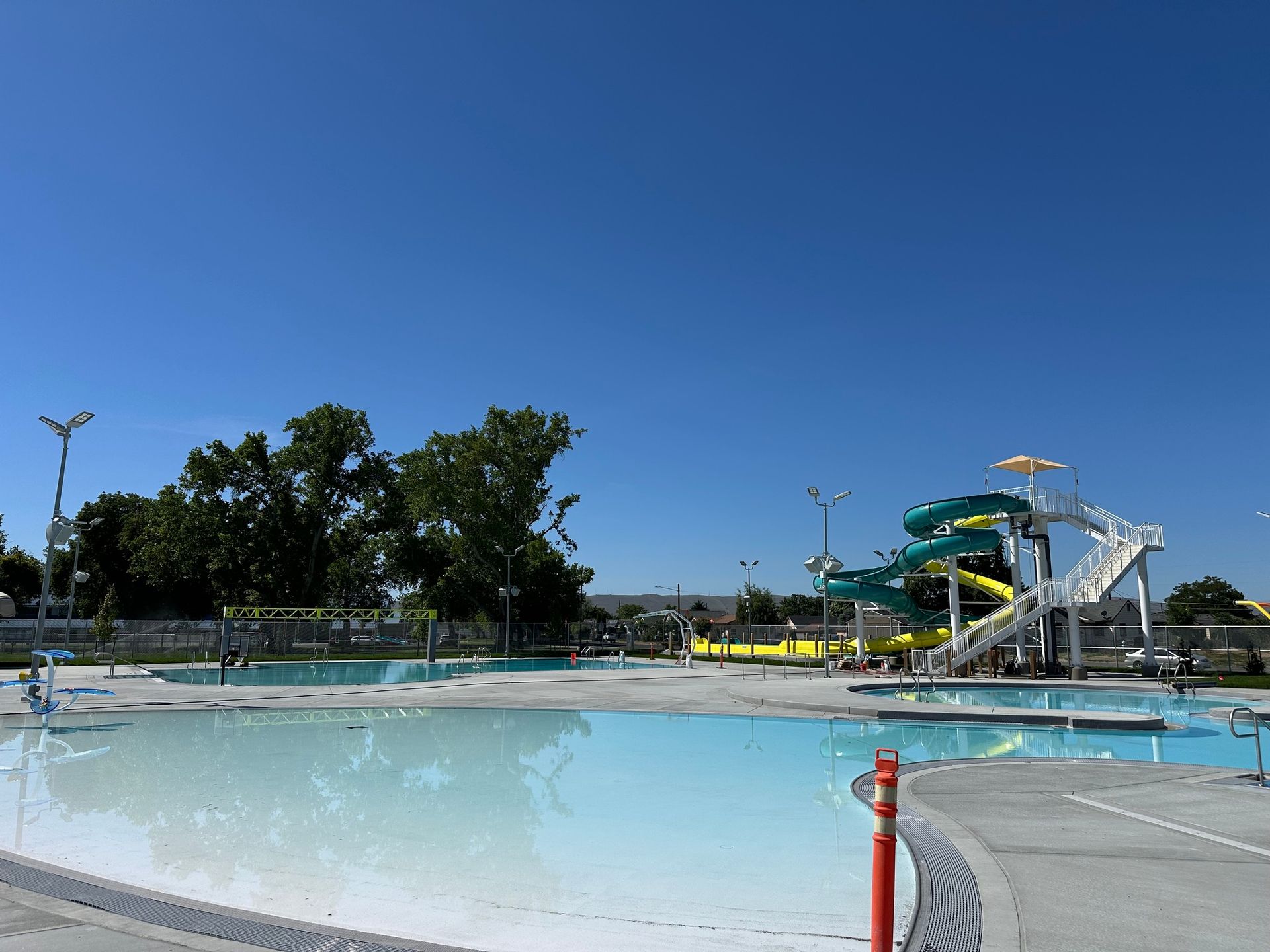Water park with a large pool, waterslides, and trees under a clear blue sky.