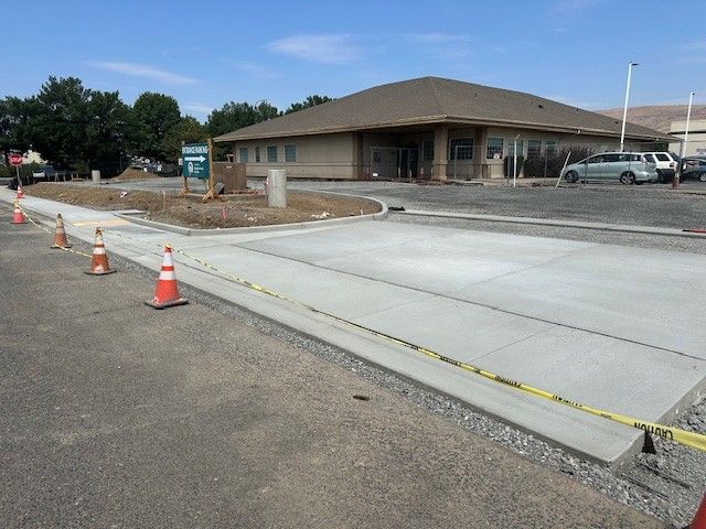 Construction site with new concrete sidewalk and orange cones in front of a tan building.