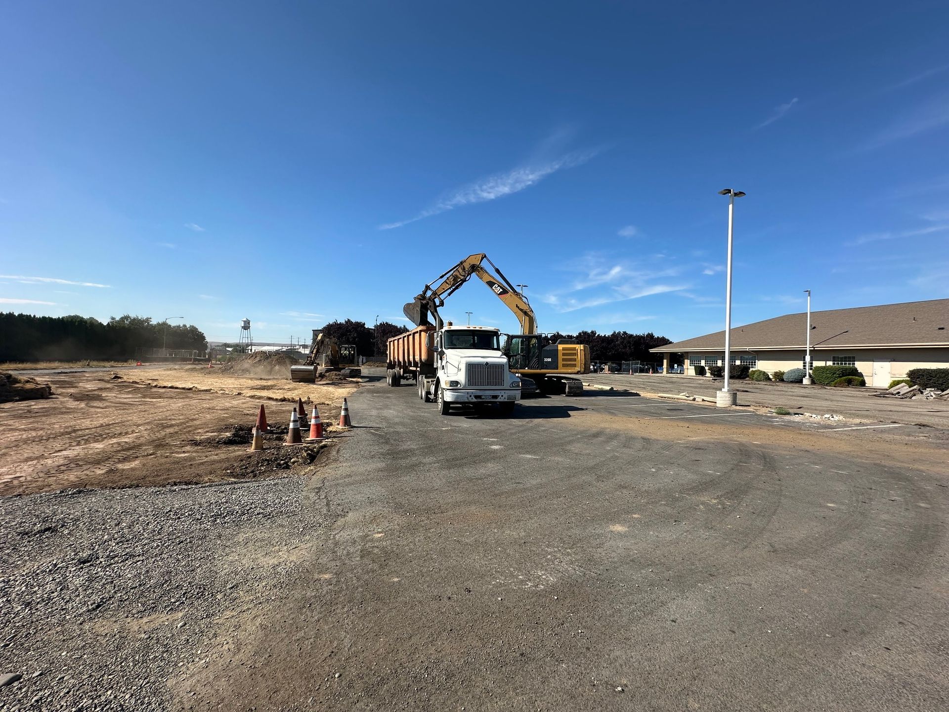 Construction site with excavator loading logs onto a truck; clear blue sky.