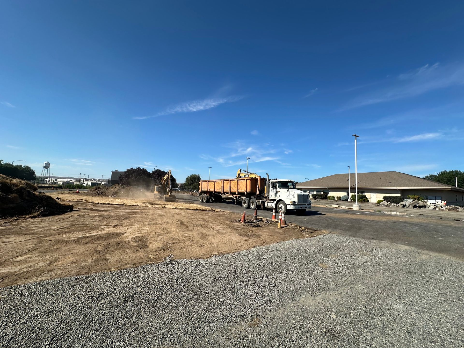 Construction site with dump truck and excavator under blue sky.