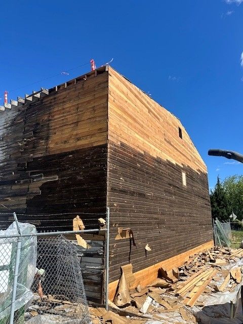 Barn in partial demolition, dark weathered wood and newer wood siding, clear blue sky.