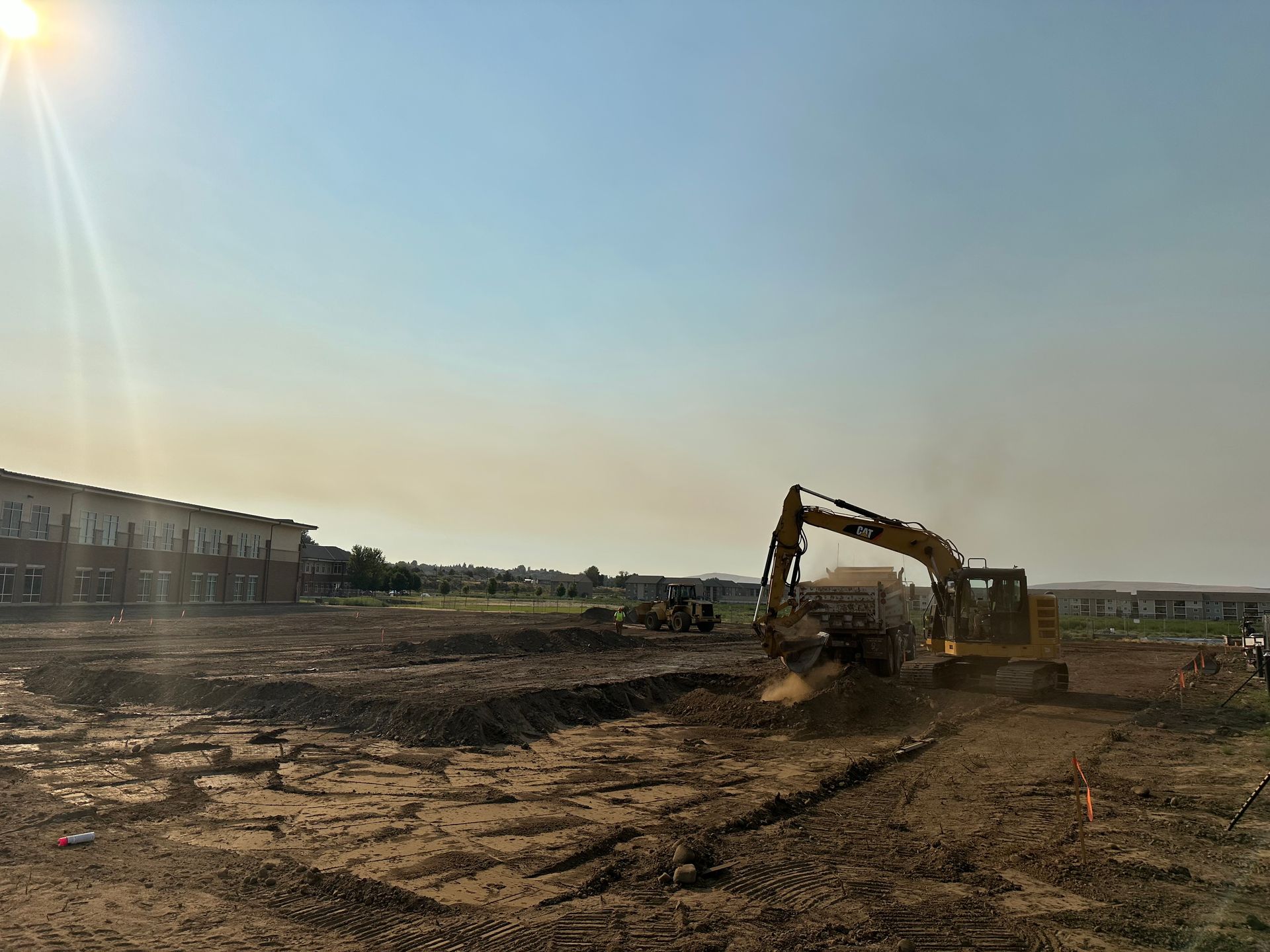 Construction site with excavator moving dirt, a partially built building, and blue sky.