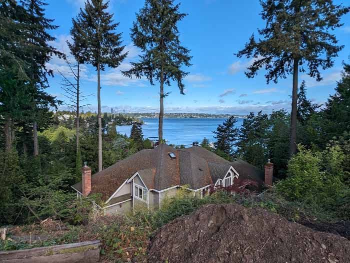 House nestled among tall trees, overlooking a body of water on a partly cloudy day.
