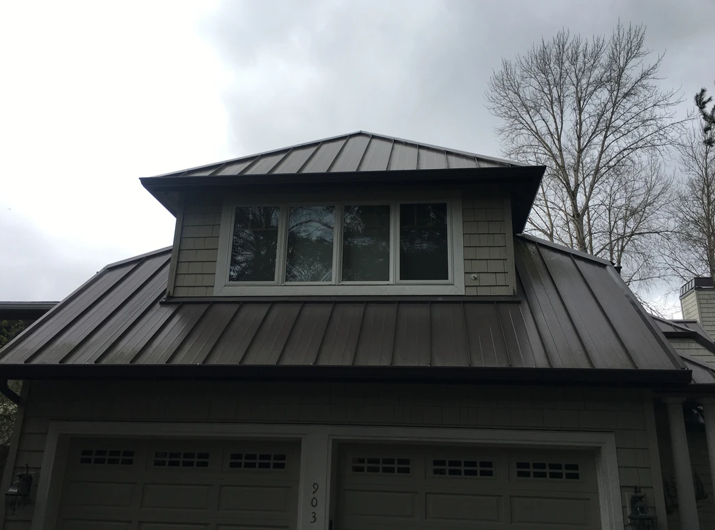 Garage with brown metal roof, dormer with white windows, cloudy sky.