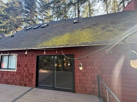 Red-sided house with a mossy roof, string lights, and a deck. Trees are in the background.