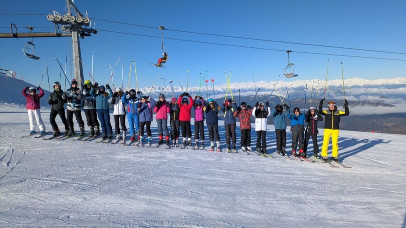 Un gruppo di bambini e adulti sta lanciando palloni da basket in una palestra. I giocatori indossano uniformi rosse e blu e sembrano divertirsi.
