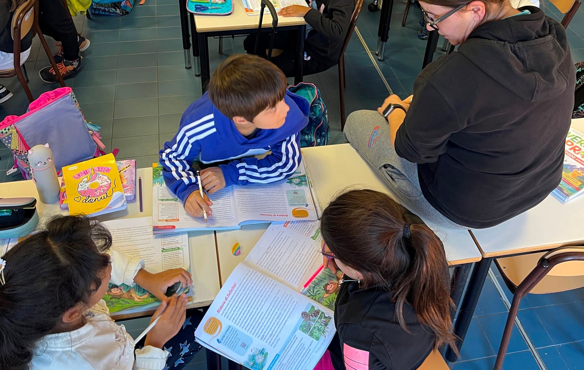 Un gruppo di bambini e adulti sta lanciando palloni da basket in una palestra. I giocatori indossano uniformi rosse e blu e sembrano divertirsi.