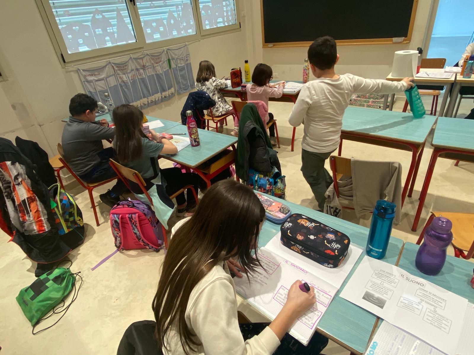 Un gruppo di bambini e adulti sta lanciando palloni da basket in una palestra. I giocatori indossano uniformi rosse e blu e sembrano divertirsi.