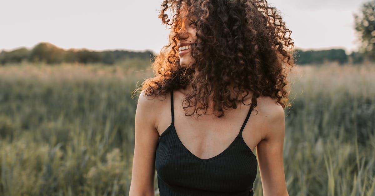 A woman with curly hair is standing in a field wearing a black tank top.