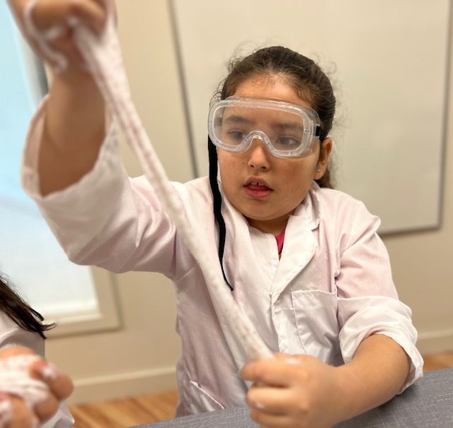 Montessori child in a lab coat and goggles is working with slime