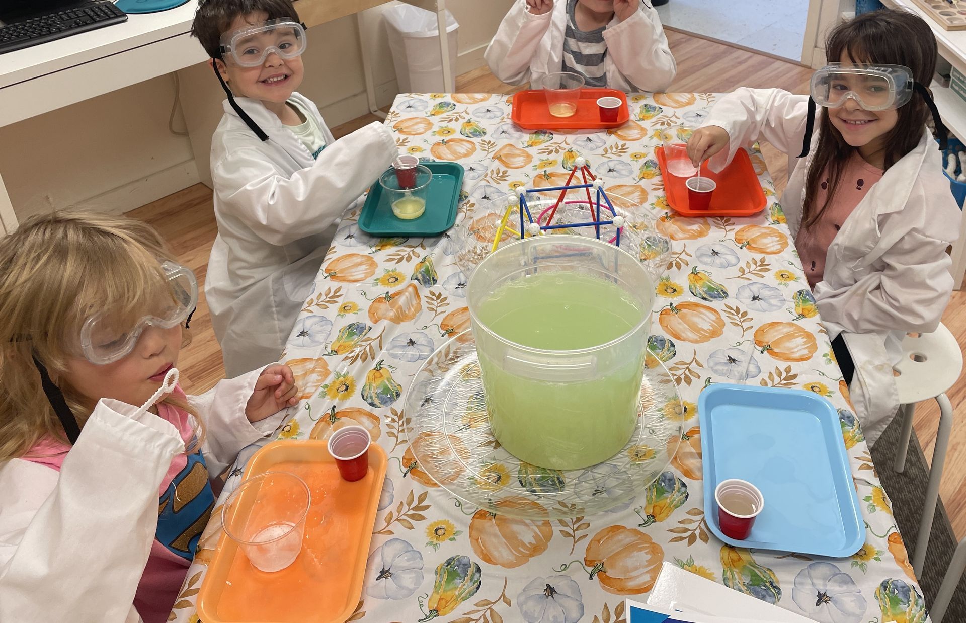 Montessori children wearing lab coats and goggles are sitting at a table.