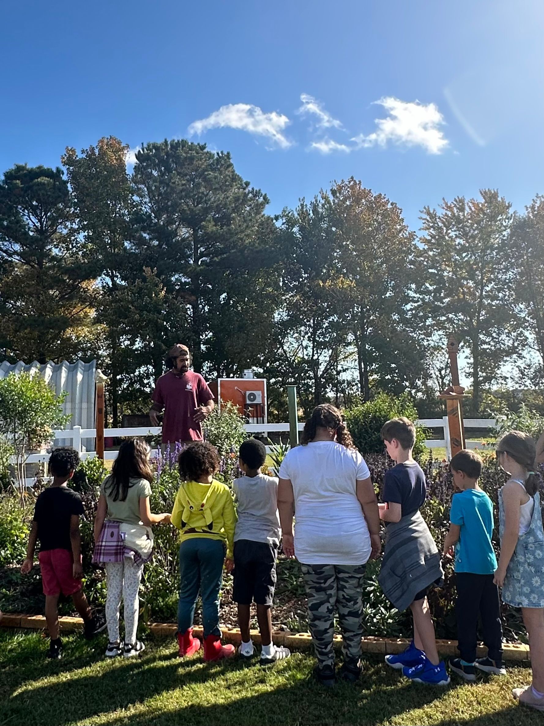 A Montessori guide holding a plant in front of a group of children.
