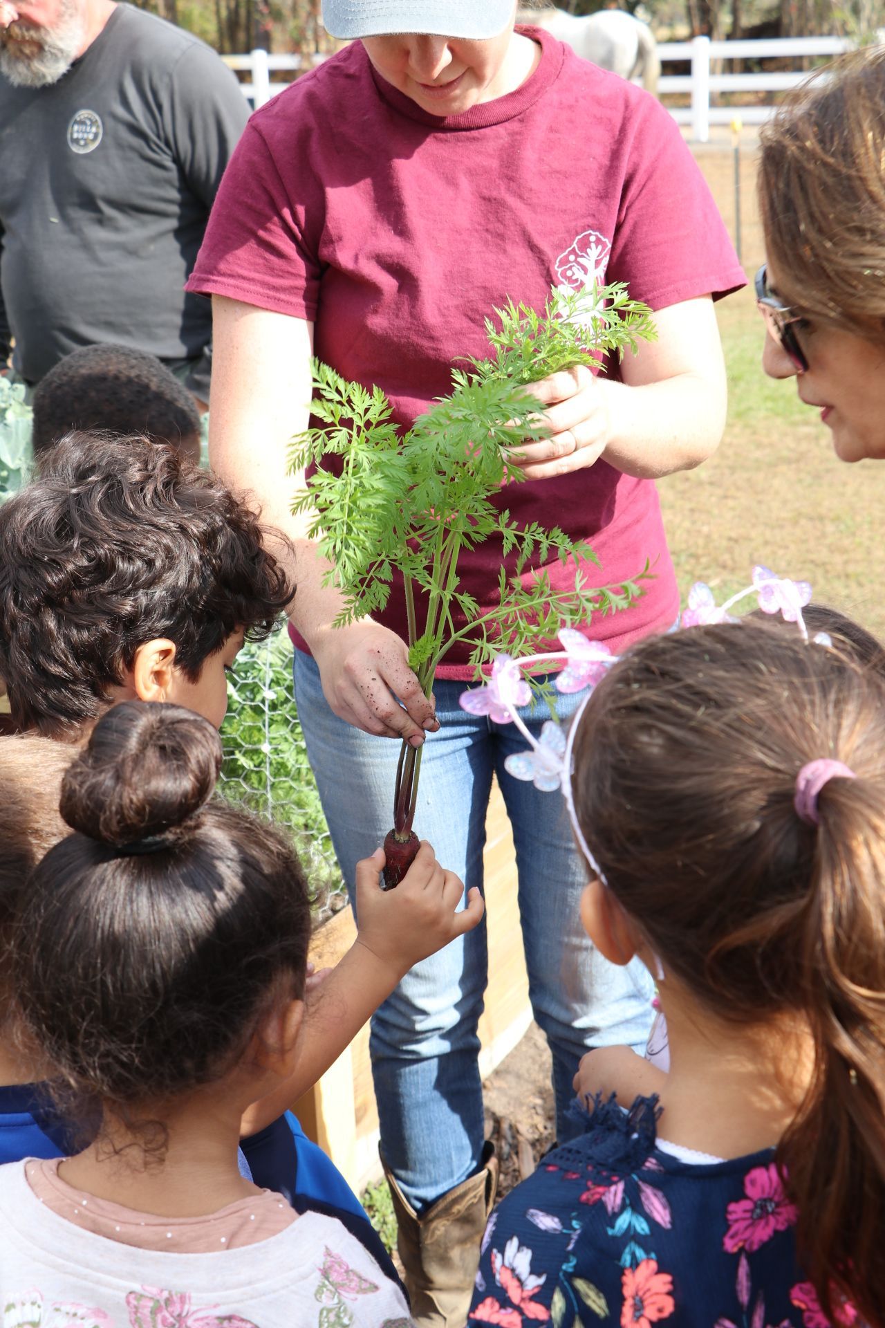 A Montessori guide is holding a plant in front of a group of children.